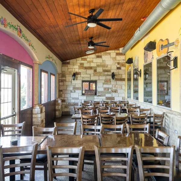 Empty restaurant dining room with wooden tables and chairs, stone walls, and a wooden ceiling with fans.