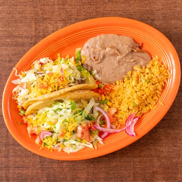 Two crispy tacos with lettuce, cheese, and tomatoes, served with refried beans and yellow rice on an orange plate.