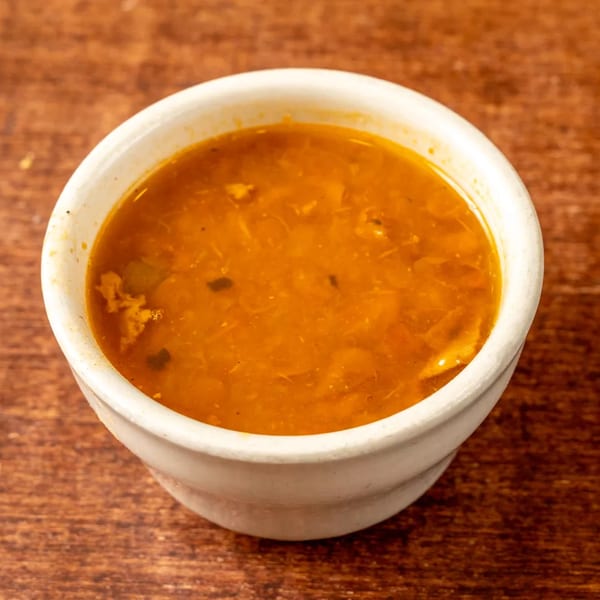 A white bowl filled with a rich, orange-brown soup, featuring visible chunks of ingredients.