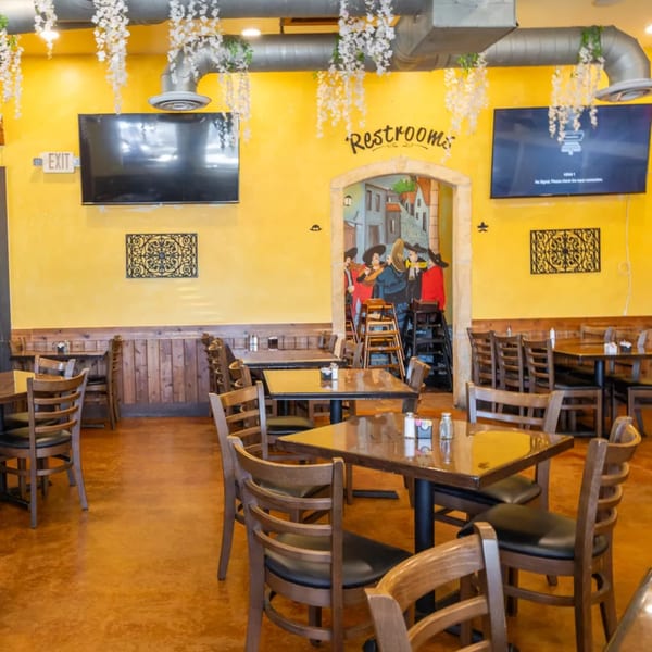Interior of Grand Tequila Mexican Restaurant with yellow walls, wooden tables, and a mural.
