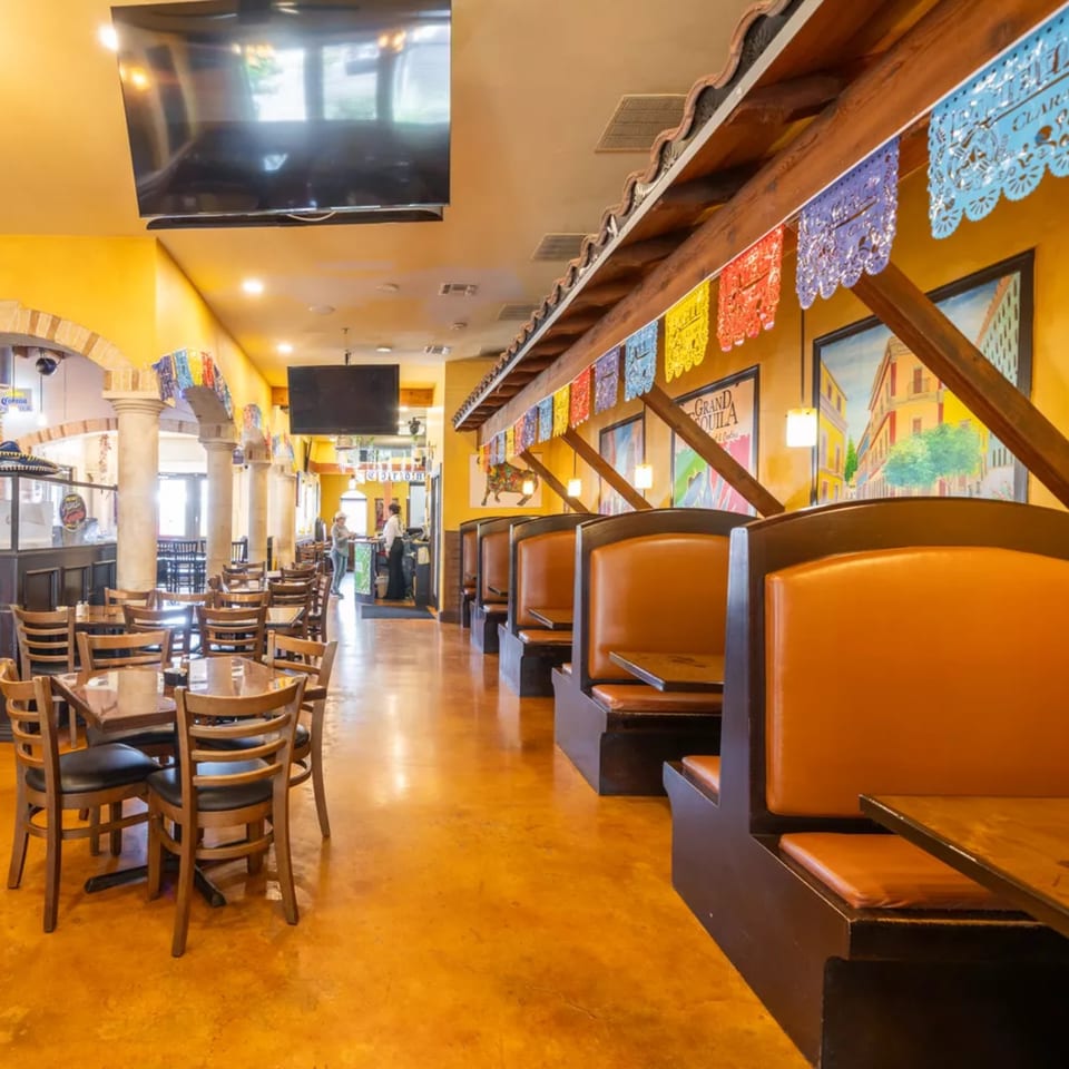 Interior of Grand Tequila Mexican Restaurant with colorful papel picado, booths, tables, and bar area.
