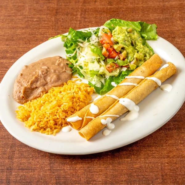 Mexican taquitos with rice, refried beans, guacamole, and salad on a white plate.
