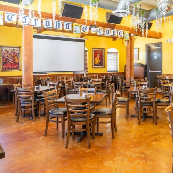 Empty restaurant dining room with yellow walls, wooden tables and chairs, and a large projection screen.