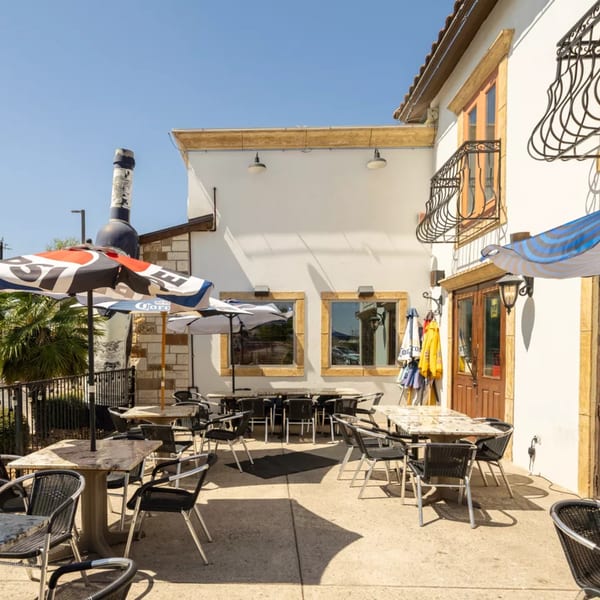 Outdoor patio of a restaurant with tables, chairs, and umbrellas under a clear sky.