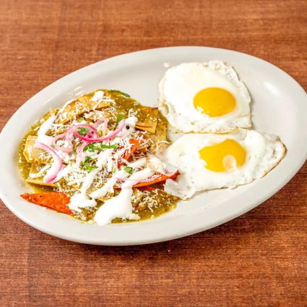 Chilaquiles with green sauce, cheese, red onions, and two fried eggs on a white plate.