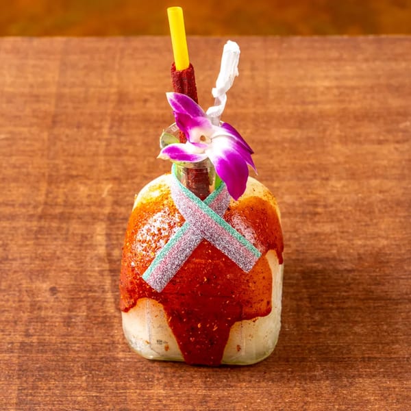 A Grand Tequila Mexican Restaurant drink in a bottle, garnished with a purple orchid and candy.