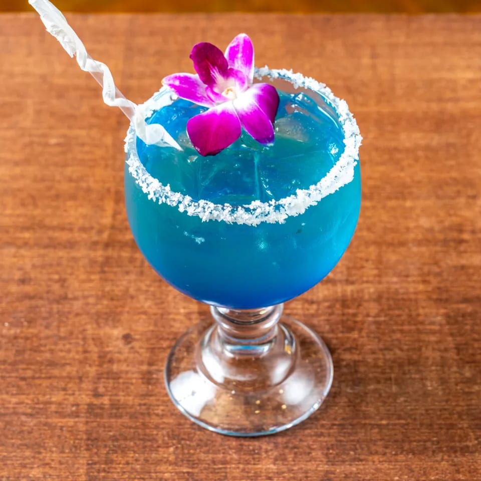 Vibrant blue cocktail with a salted rim, garnished with a purple orchid and a white straw.