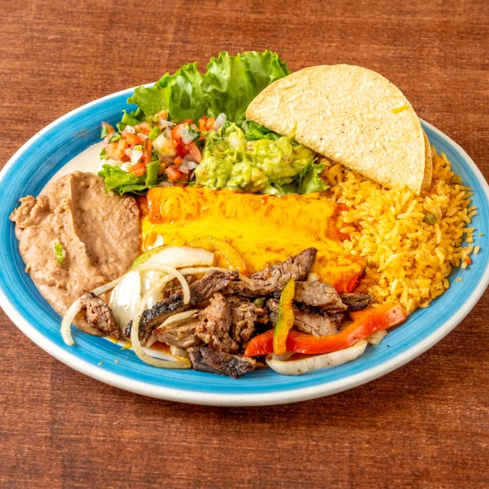 A Grand Tequila Mexican Restaurant combo plate with steak fajitas, enchilada, rice, beans, guacamole, pico de gallo, and a taco.