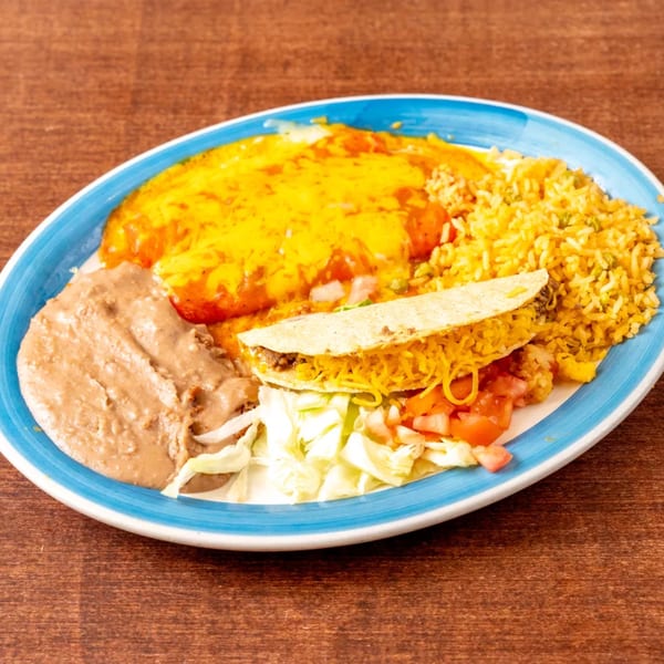 A blue and white plate holds a Mexican combination platter with a cheesy enchilada, rice, refried beans, and a taco.